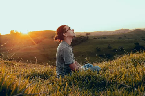 Mann mit geschlossenen Augen sitzt auf einem Grasfeld